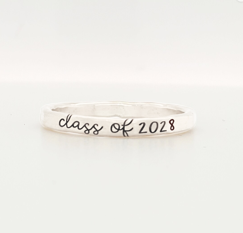 A sterling silver colored stacking ring with 'class of 2028' engraved on it, displayed against a white background.

