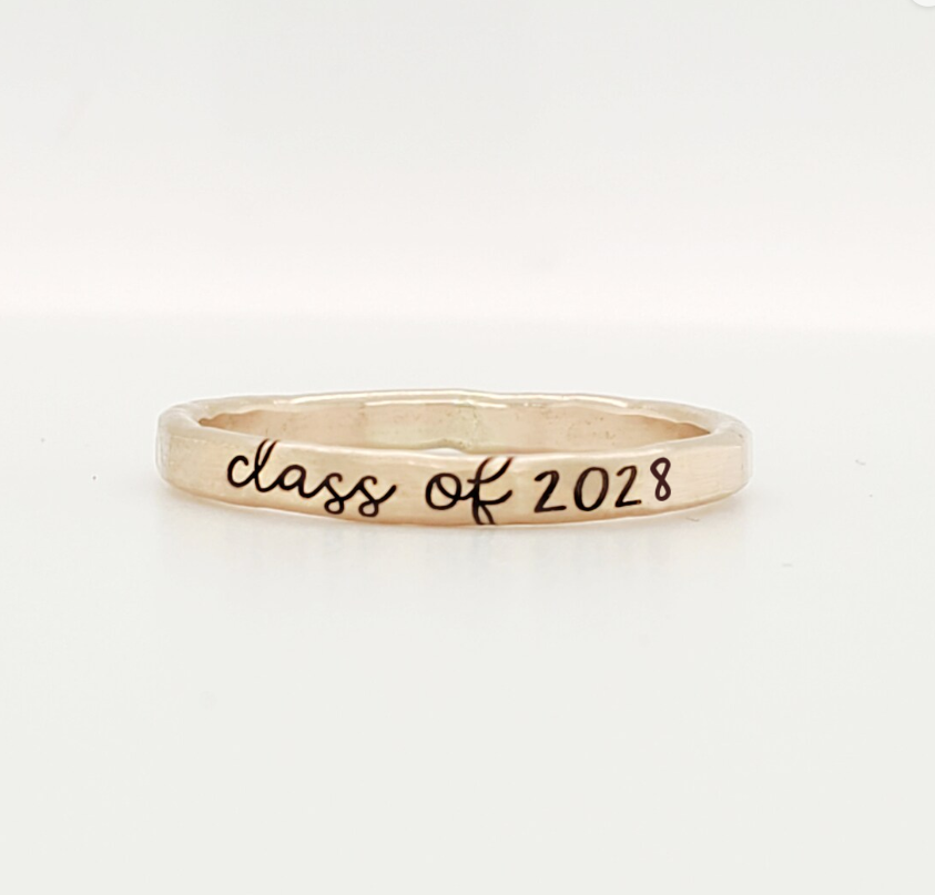 A gold-colored stacking ring with 'class of 2028' engraved on it, displayed against a white background.