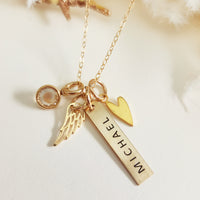 Close-up of gold engraved bar memorial necklace with “Michael” engraving, gold heart charm, angel wing charm, and clear birthstone.