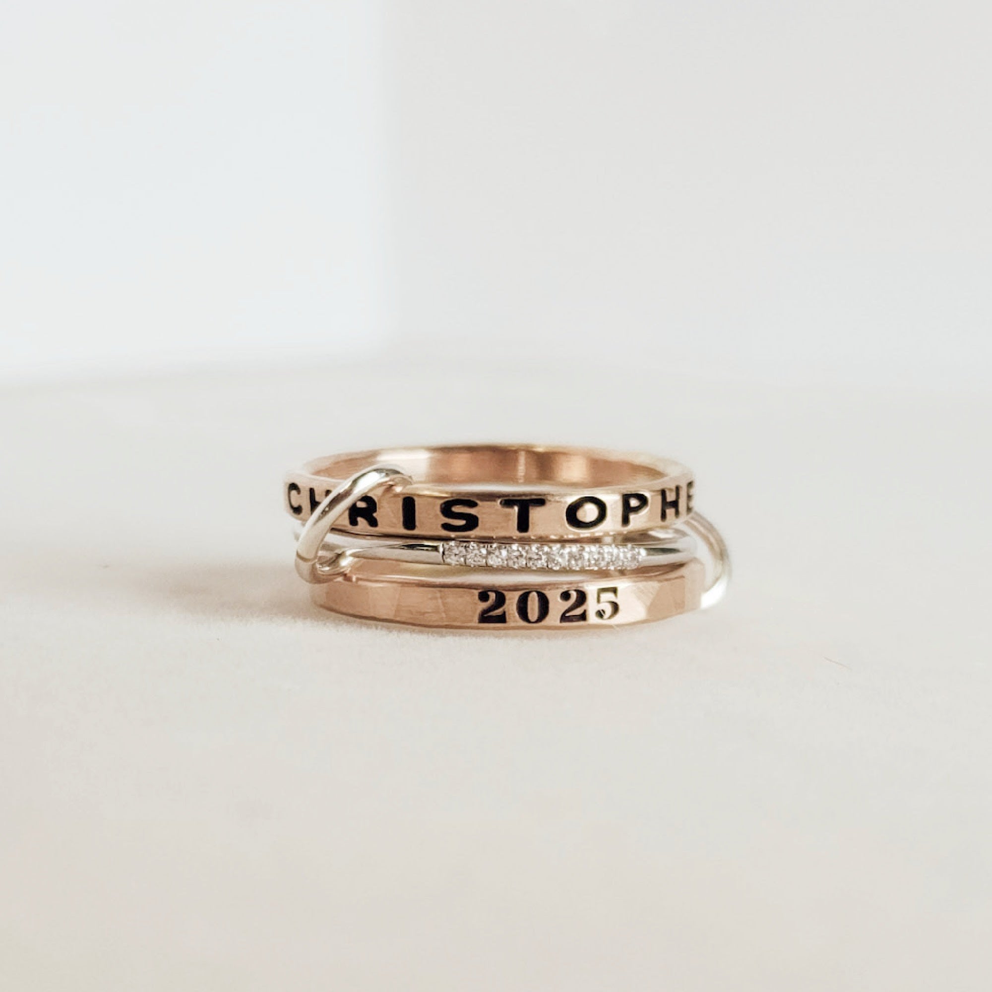 A set of personalized rings on a white background, featuring a gold-filled band with the name 'Christopher' and the year '2025' inscribed on it.
