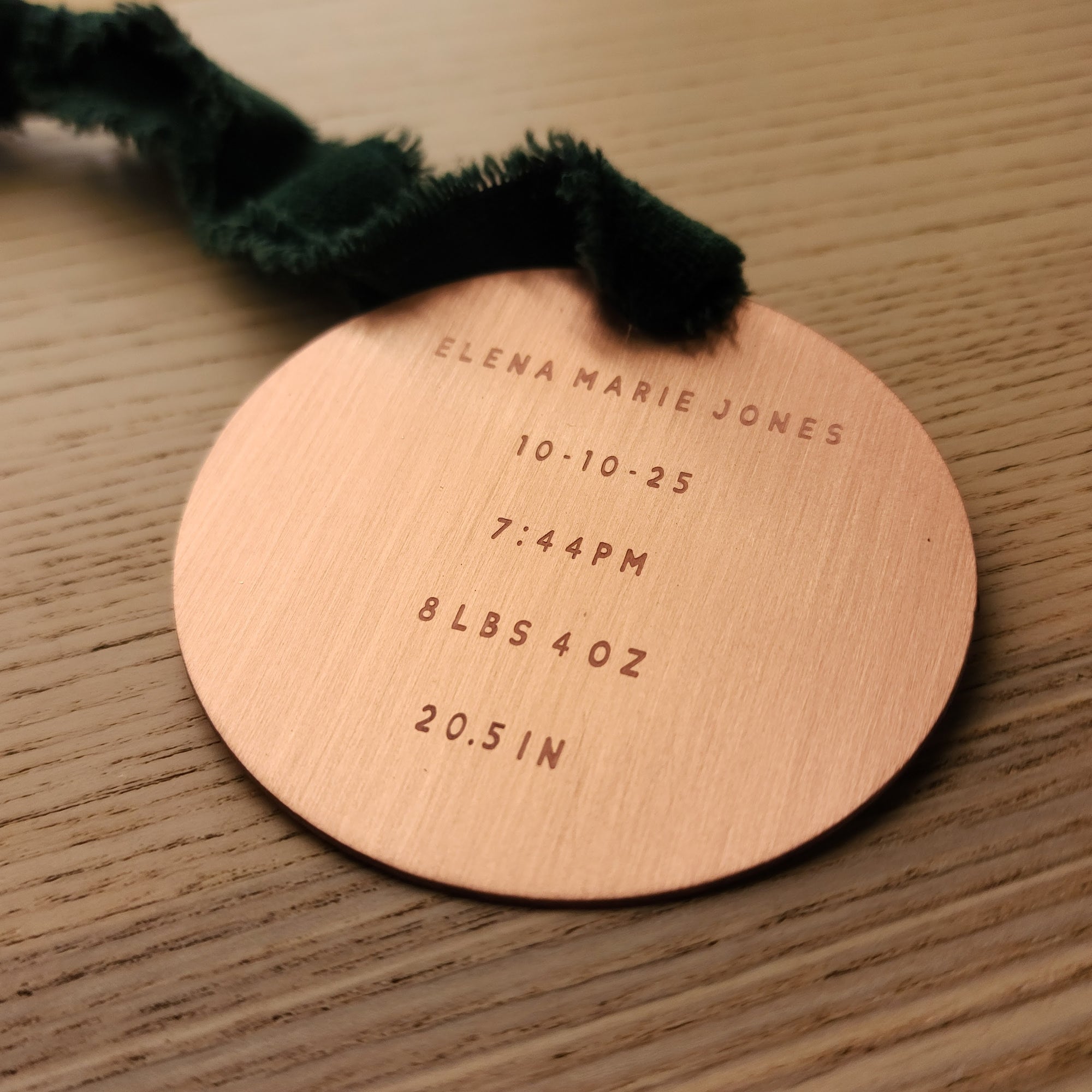 Round metal ornament with engraved birth details on a wooden surface