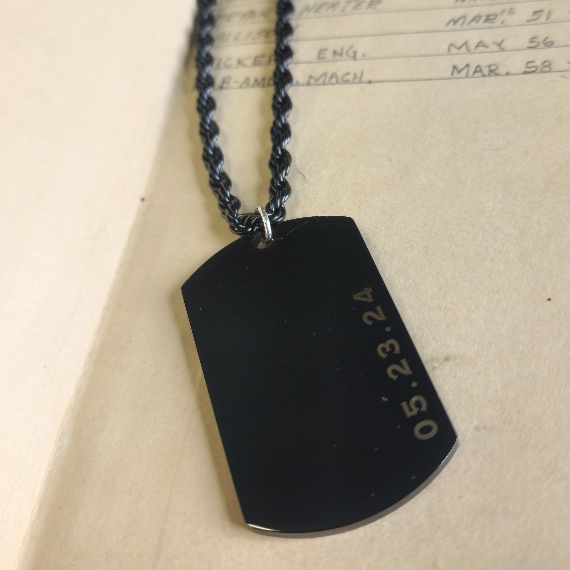 Black dog tag with engraved date on a beige background