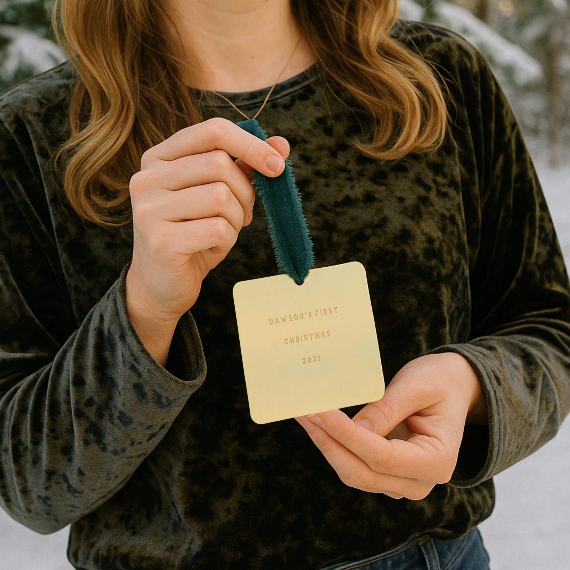 Person holding a gold ornament with text against a snowy background