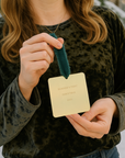 Person holding a gold ornament with text against a snowy background