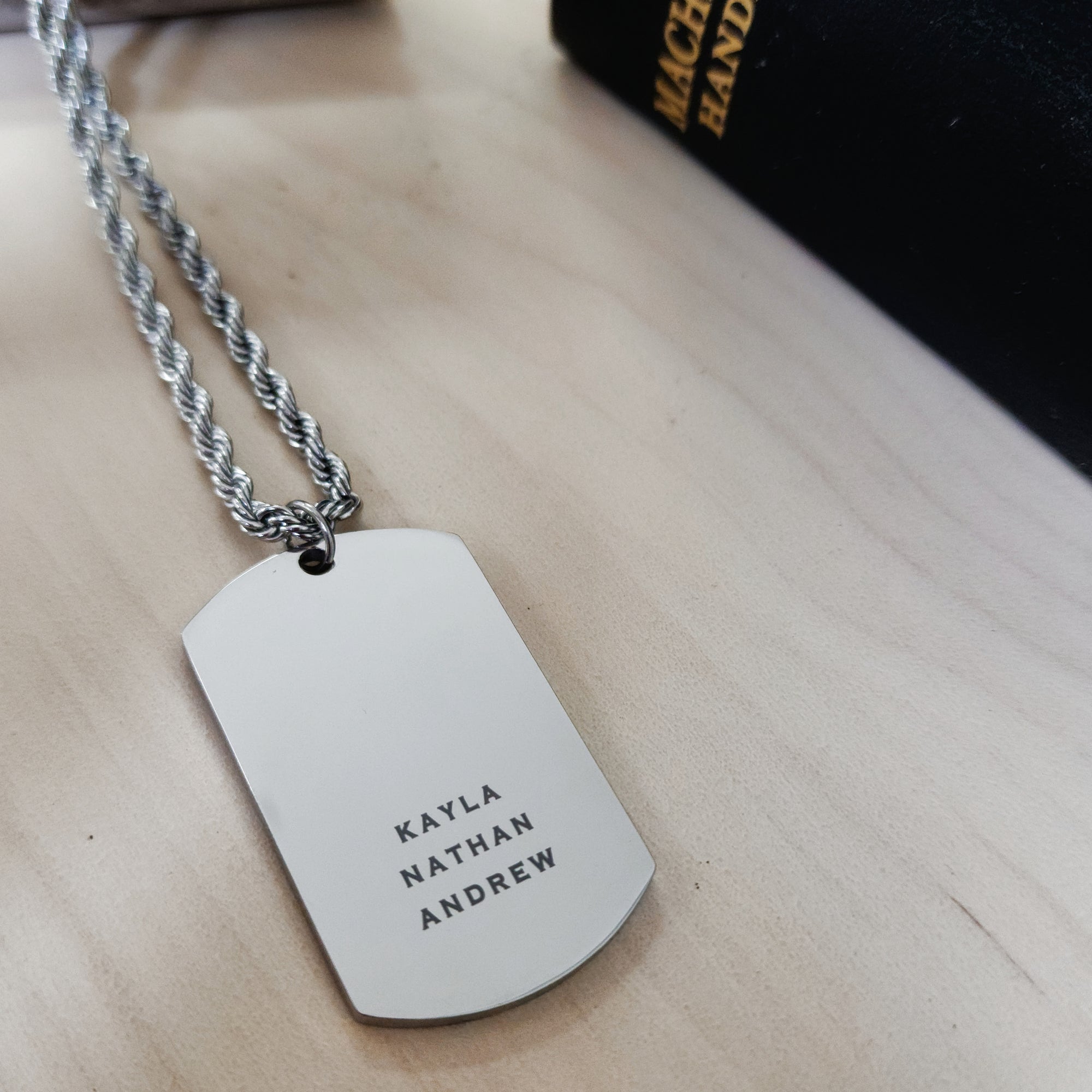 Personalized dog tag necklace with engraved names on a wooden surface