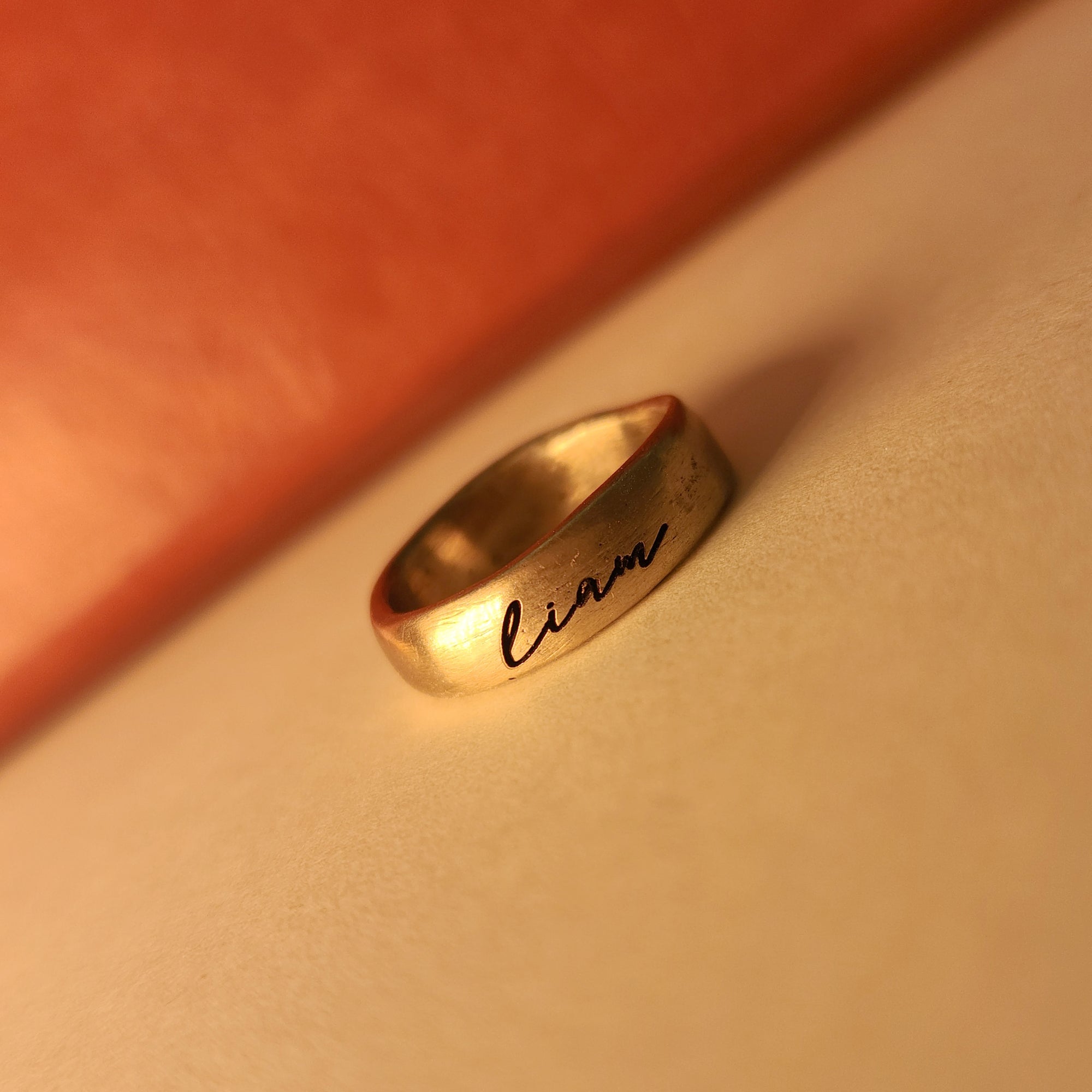 Gold ring with &#39;liam&#39; engraving on a beige surface
