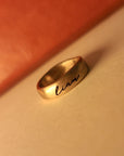 Gold ring with 'liam' engraving on a beige surface