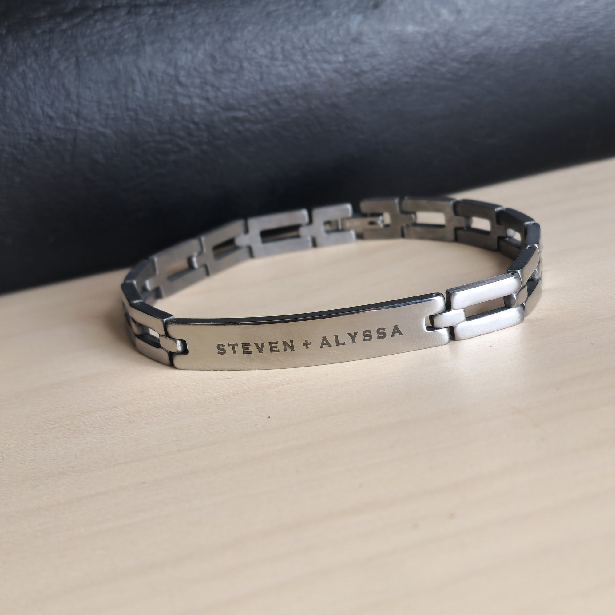Silver bracelet with engraved names on a beige surface