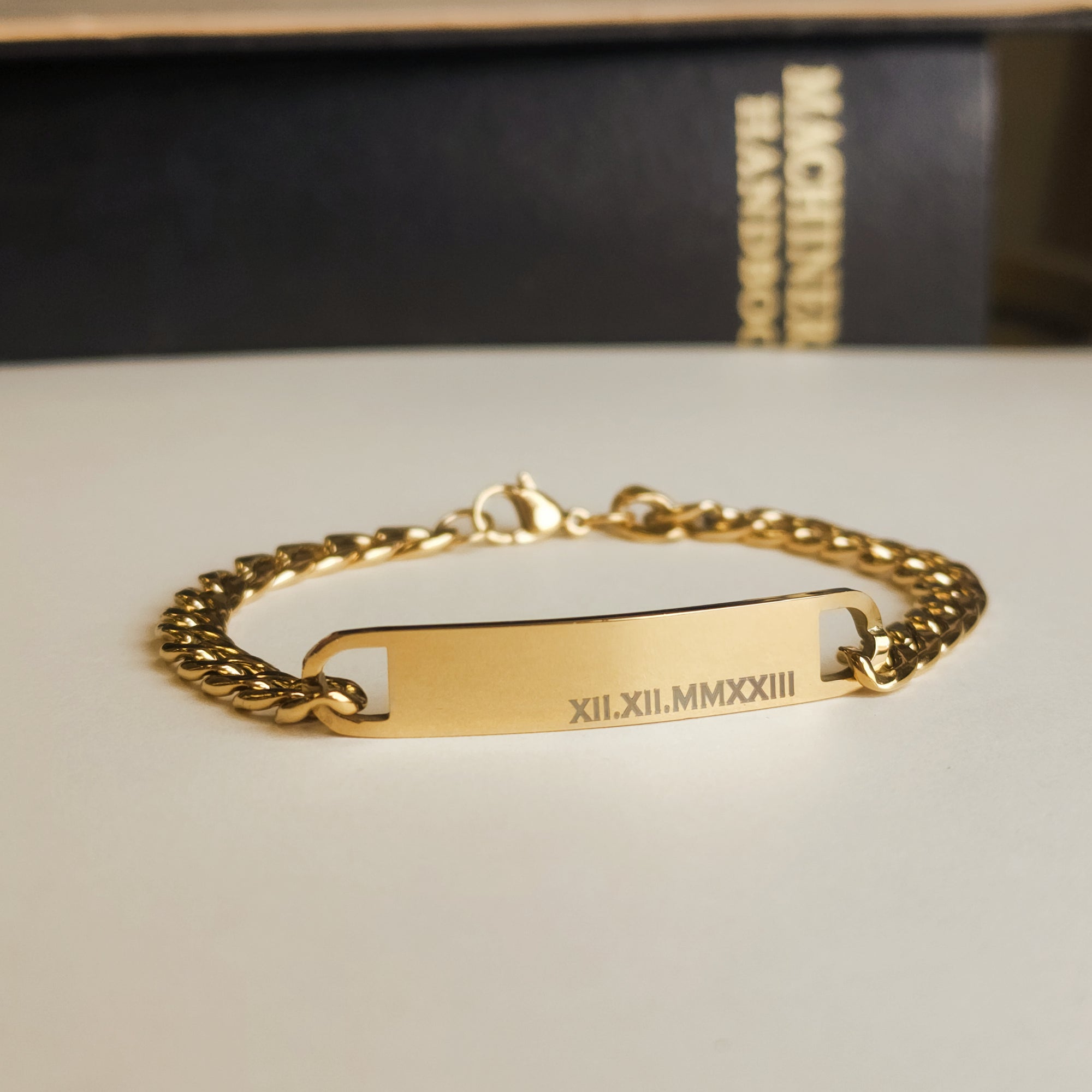 Gold chain bracelet with engraved text on a neutral background
