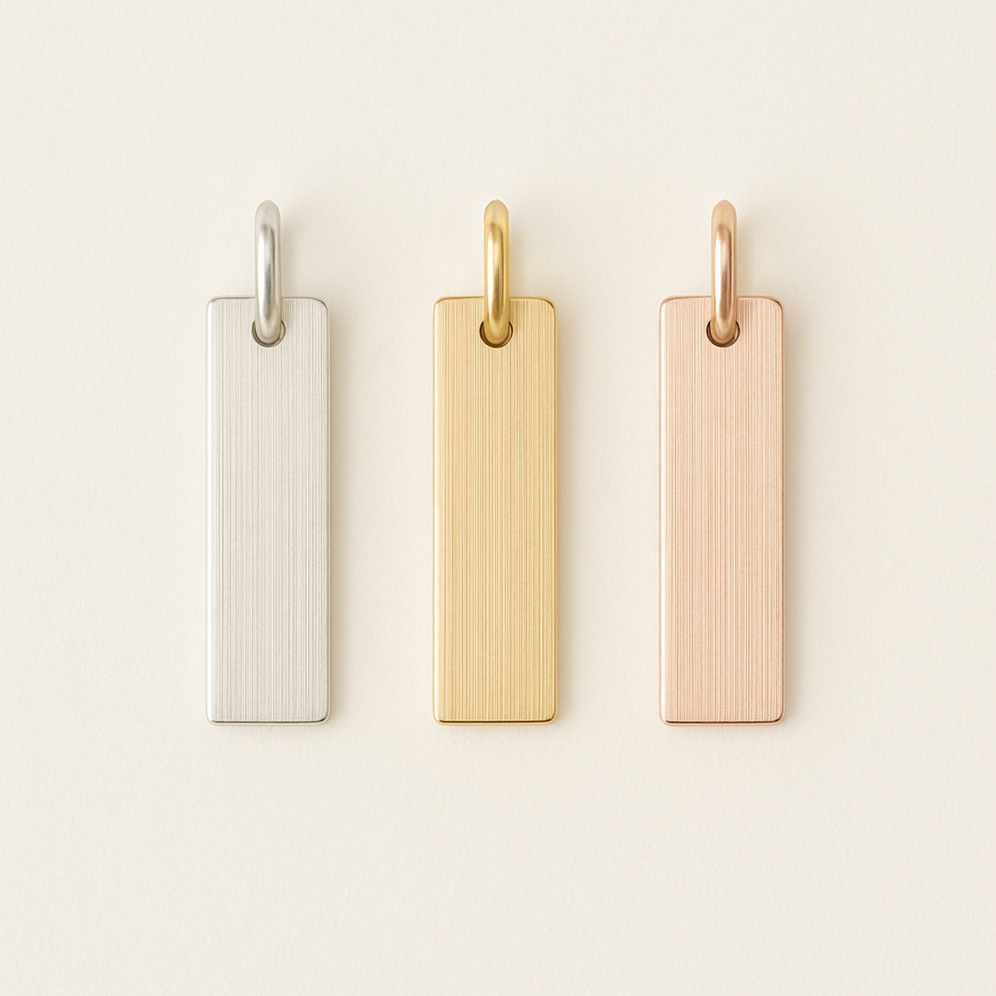 Three rectangular metal tags in silver, gold, and rose gold on a light beige background.