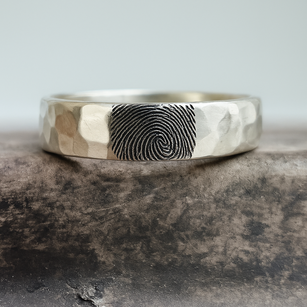 Silver ring with fingerprint engraving on a stone surface