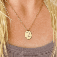 Gold necklace with a pendant on a person wearing a purple top.