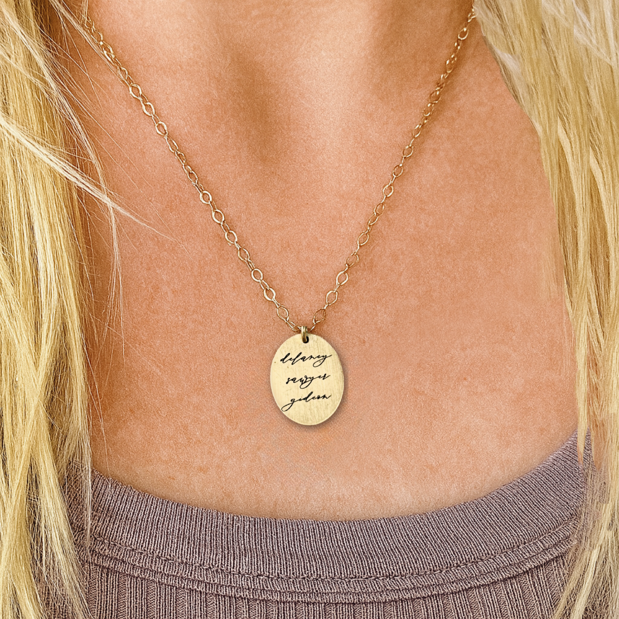 Gold necklace with a pendant on a person wearing a purple top.