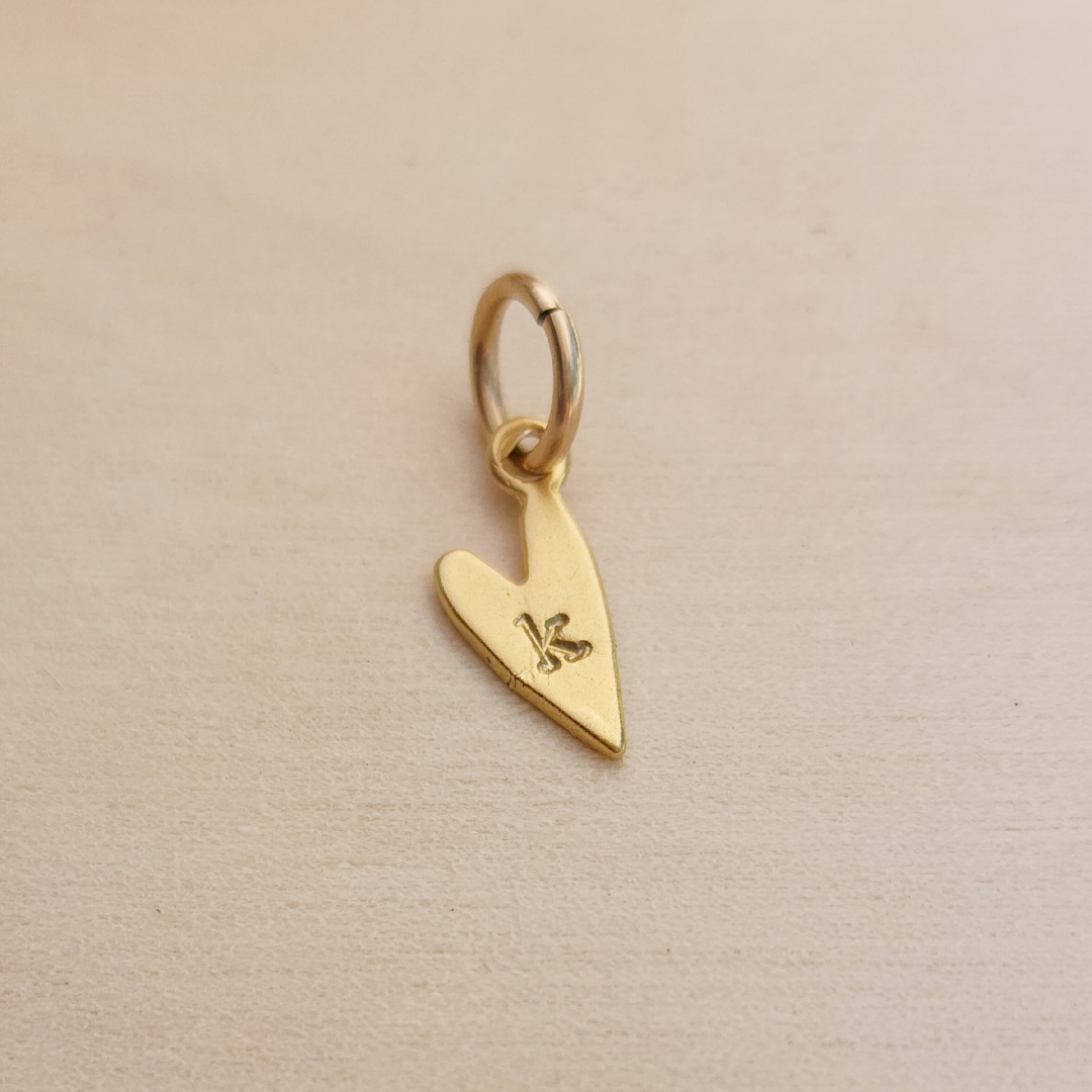Gold heart-shaped pendant with a letter &#39;K&#39; on a beige background