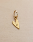 Gold heart-shaped pendant with a letter 'K' on a beige background