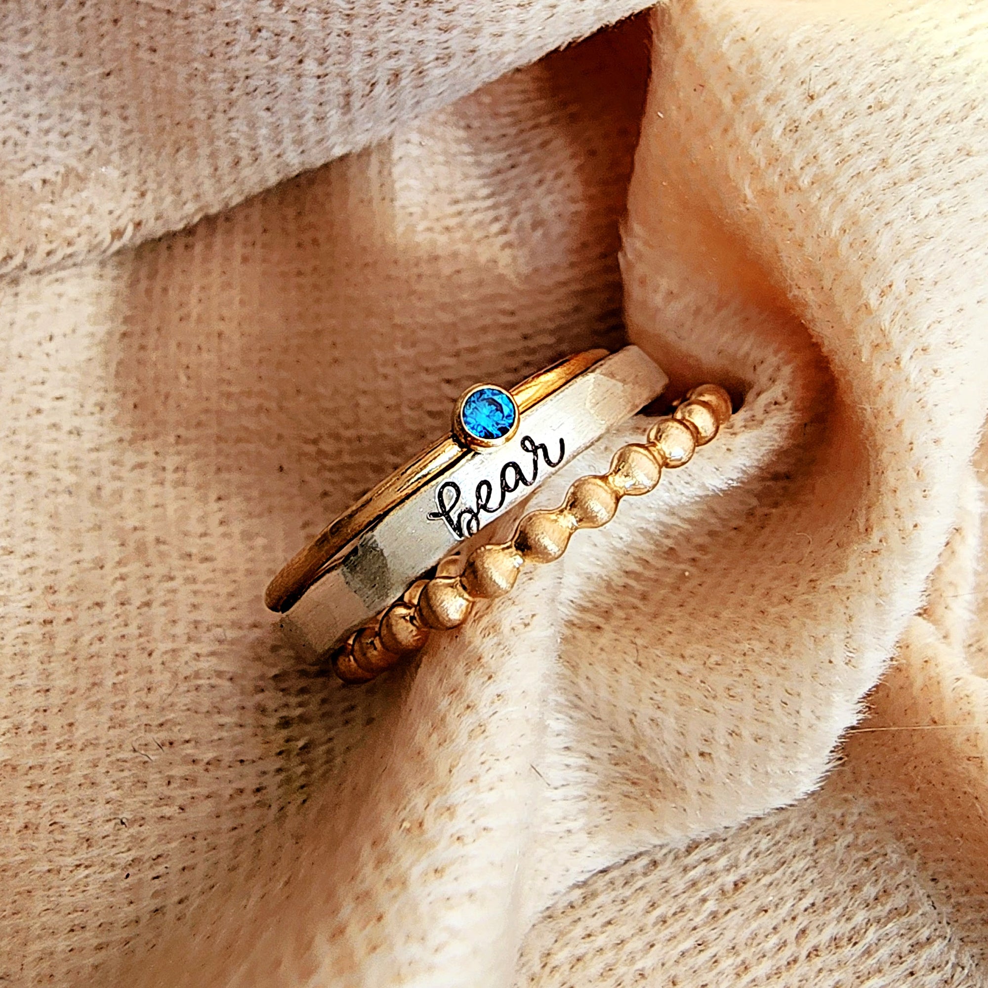 Gold ring with blue gemstone and 'bear' engraving on beige fabric