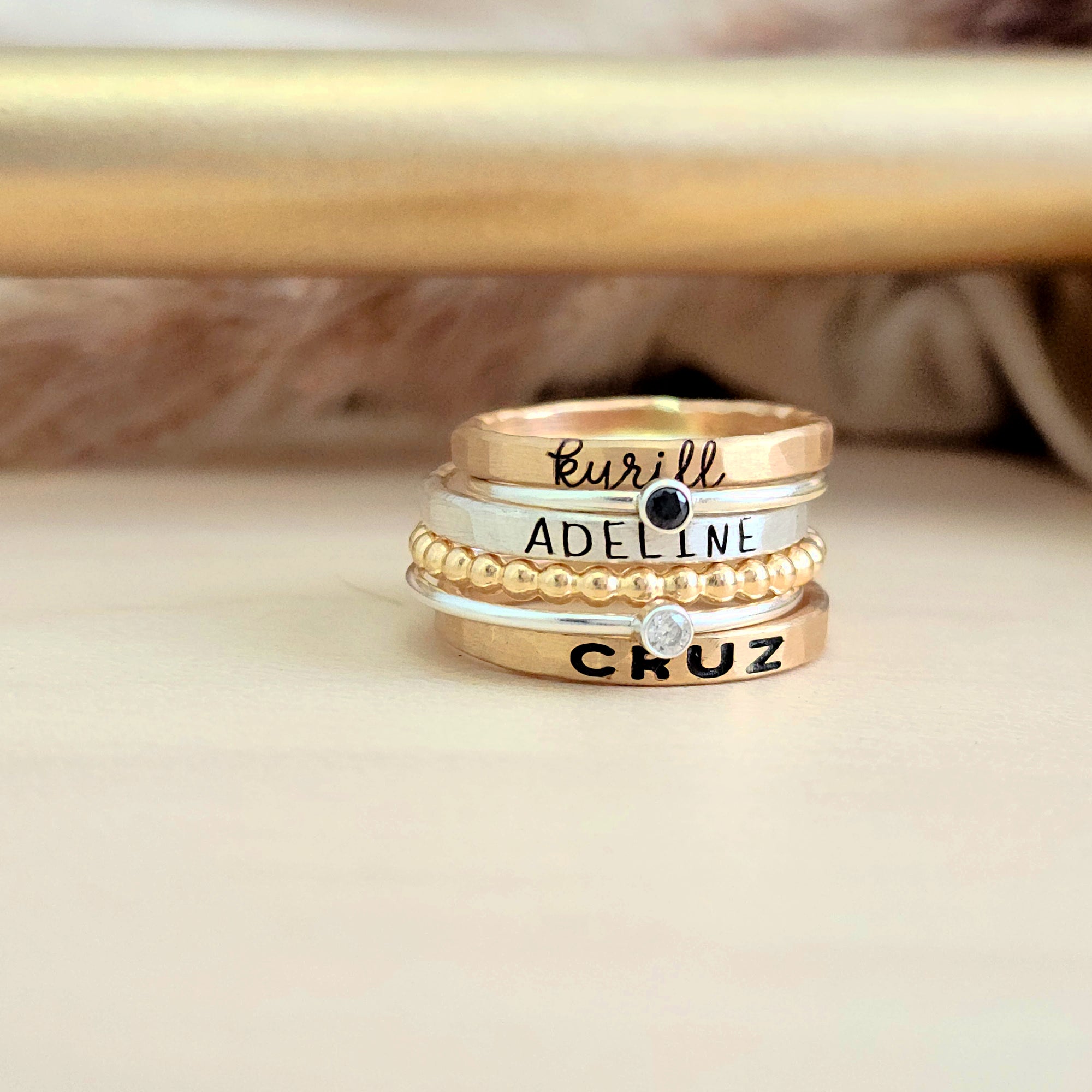 A set of mixed metal stacking name rings with personalized engravings on each ring, displayed on a person's hand.
