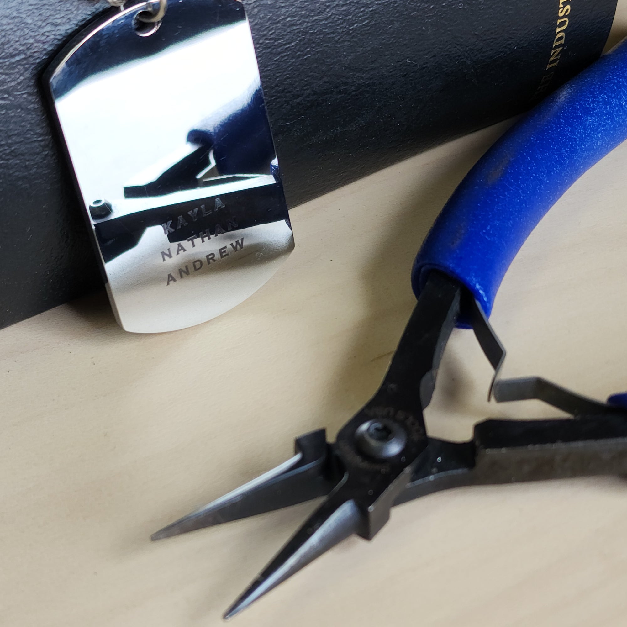 Pair of pliers with blue handle on a beige surface, next to a metal tag.