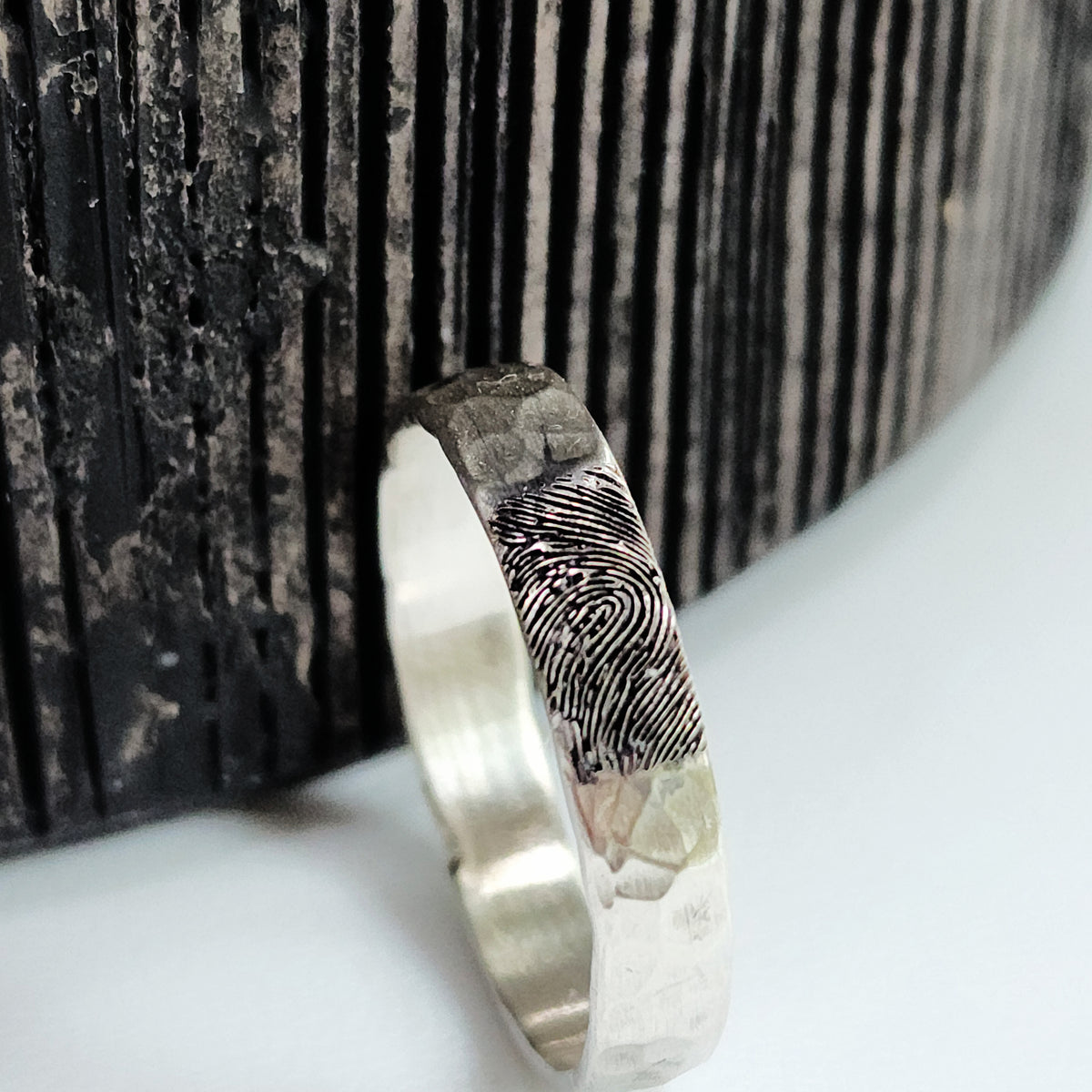 Silver ring with fingerprint design on a textured surface