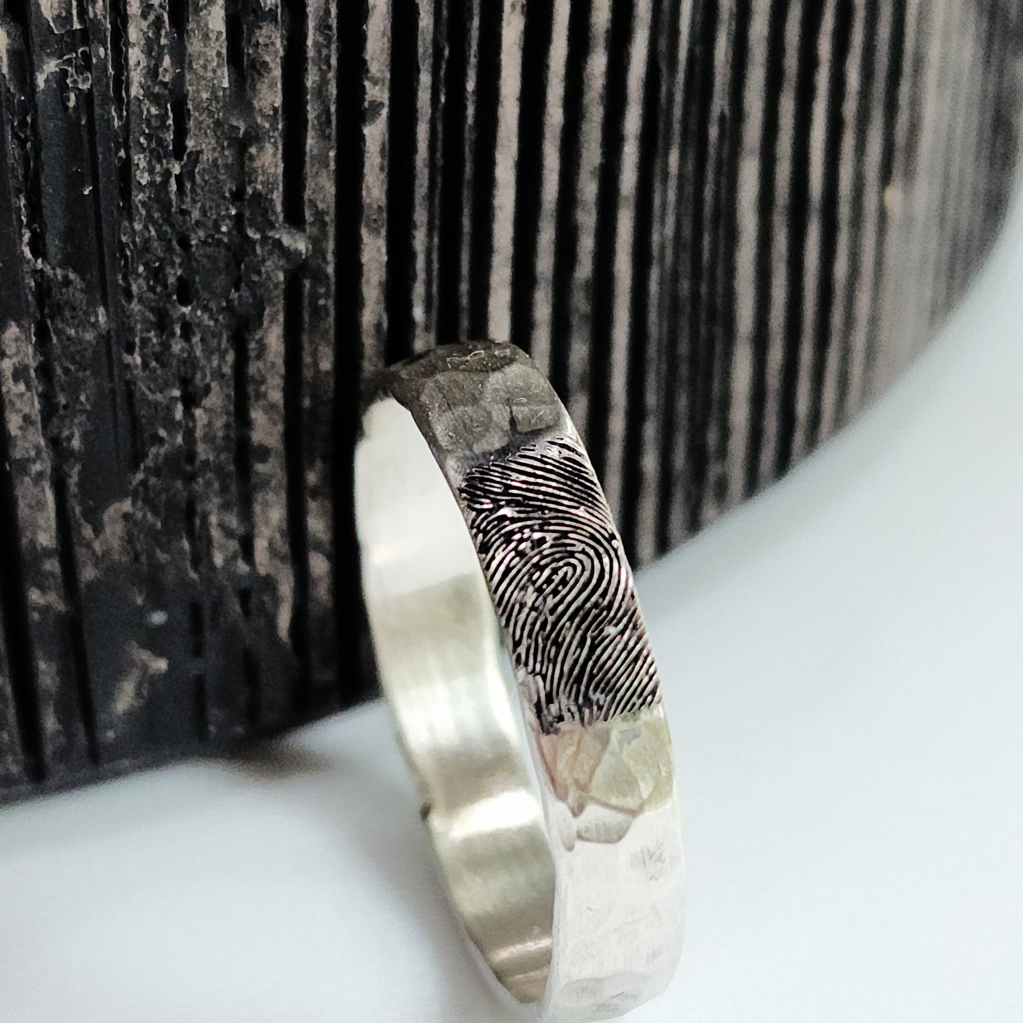 Silver ring with fingerprint design on a textured surface