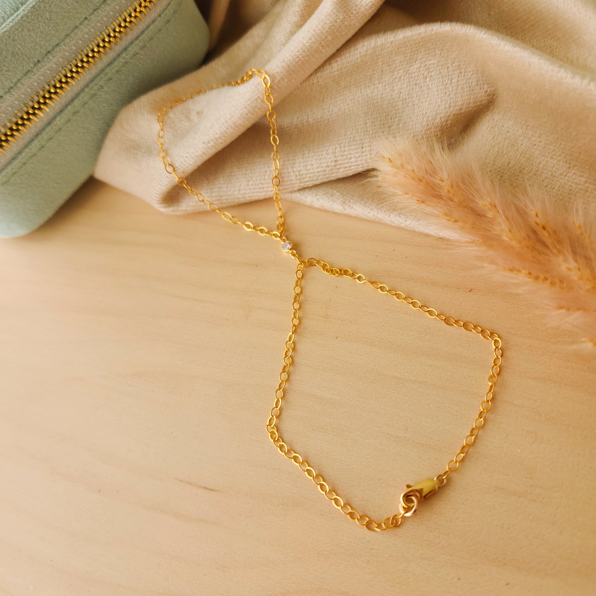 14k Gold-filled hand chain on a wooden surface with a beige fabric background