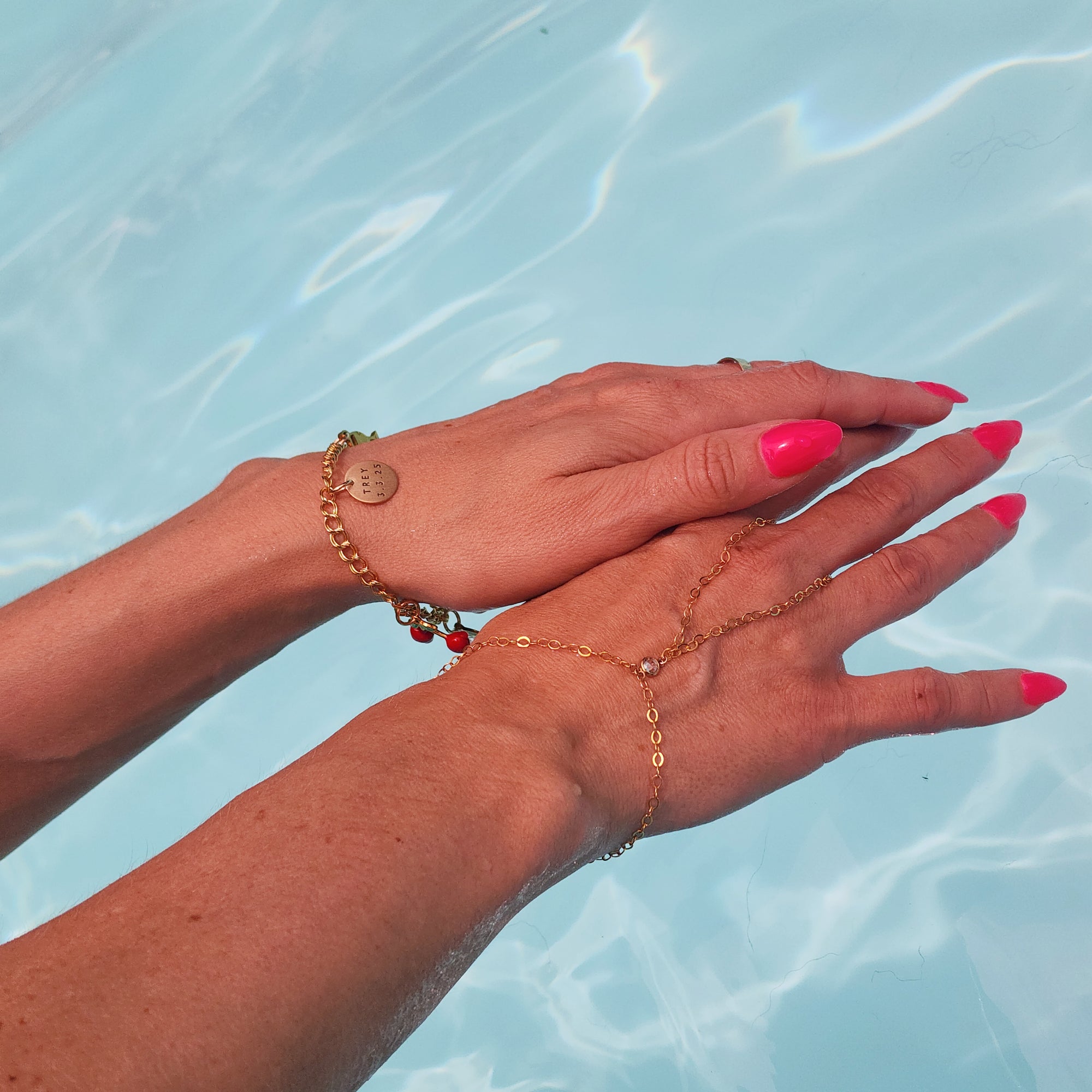 Close-up of hands with gold bracelets against a blue water background