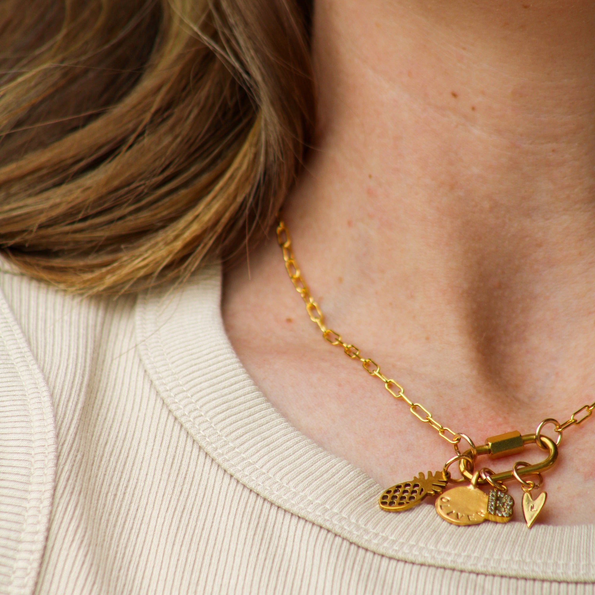 Gold necklace with charms worn by a person against a neutral background