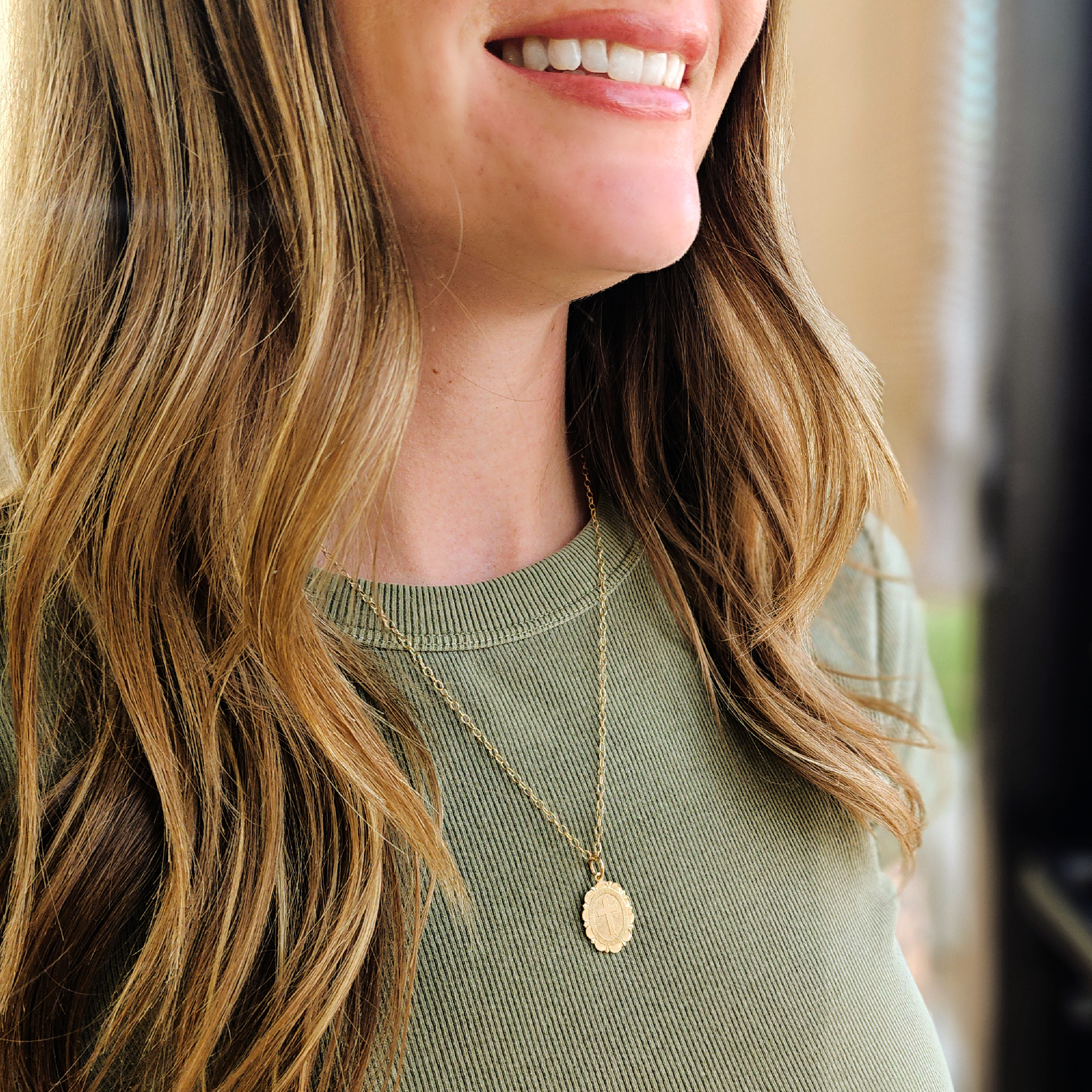 Woman wearing a gold necklace with a pendant, smiling.