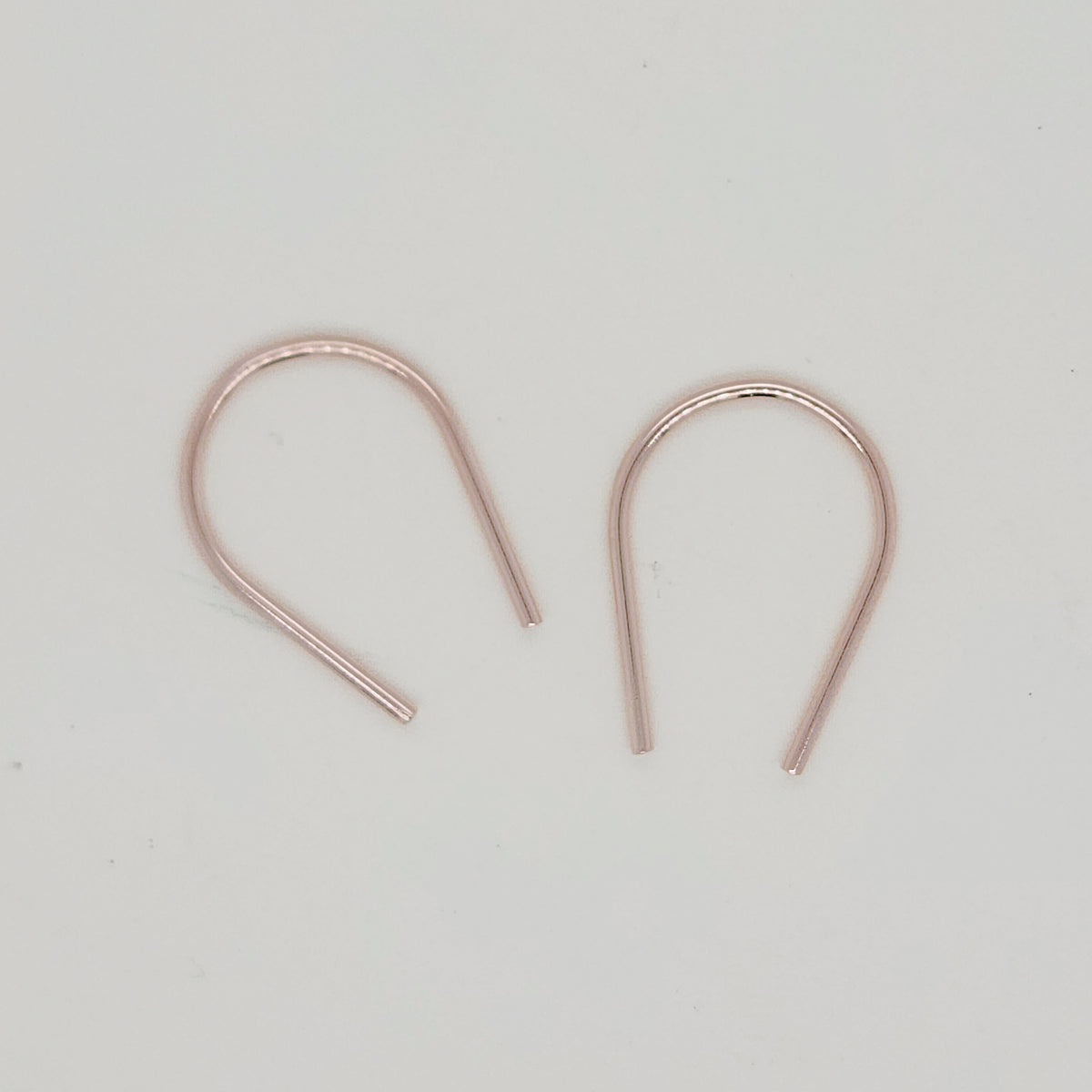 Dainty gold U-shaped earrings flat lay on cream surface