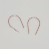 Dainty gold U-shaped earrings flat lay on cream surface