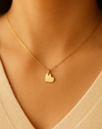 Gold heart necklace on a person wearing a beige top