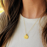 Gold necklace with a round pendant worn by a person against a neutral background