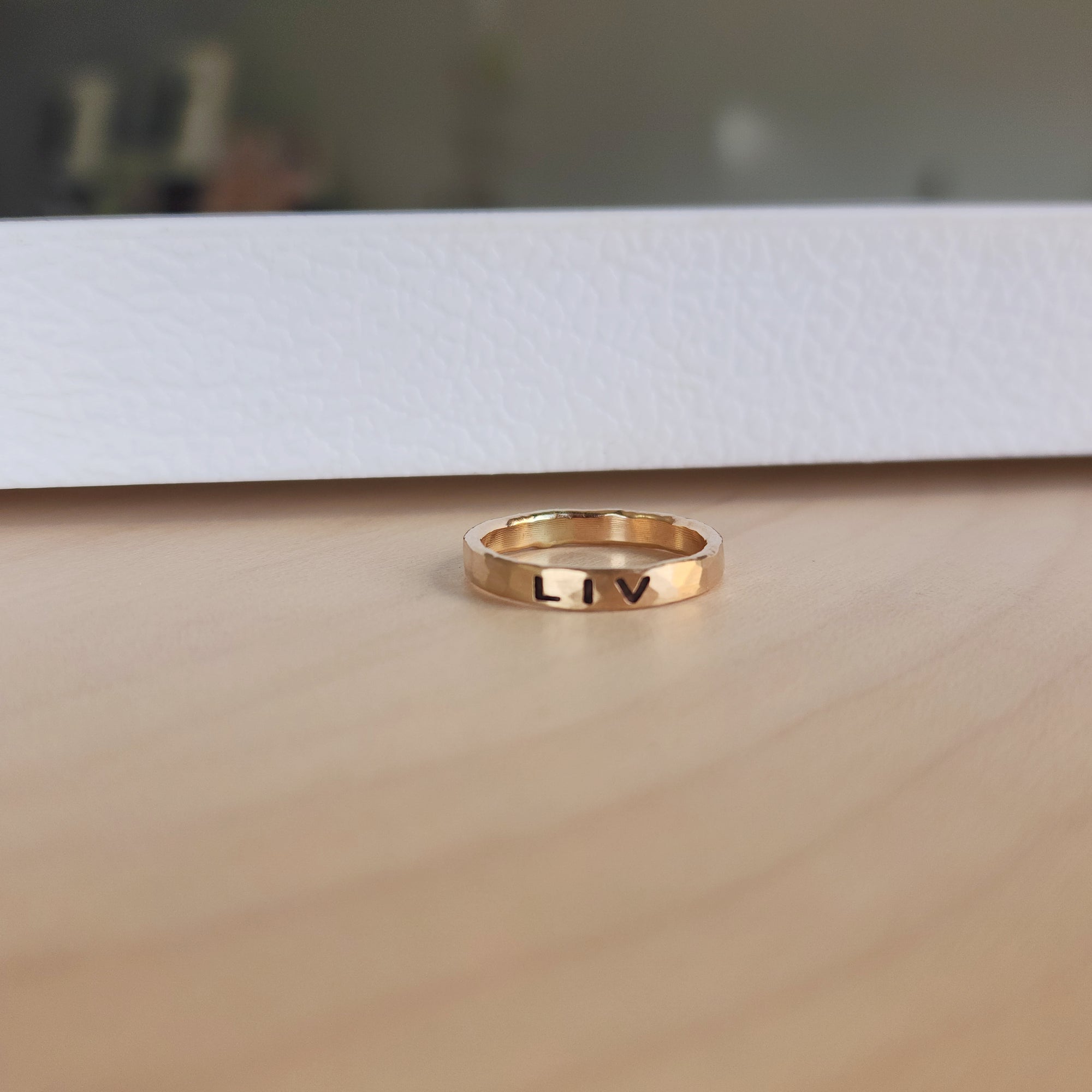 A gold filled personalized stacking ring with the name 'liv\ engraved on it, displayed on a wooden surface.