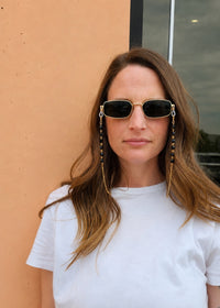 Woman wearing sunglasses with chain straps against a beige wall