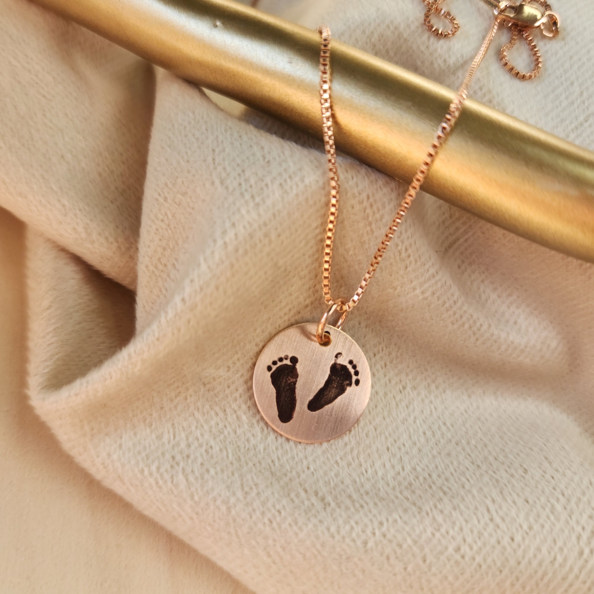 A person wearing a grey sweater and a necklace with an engraved footprint pendant on a chain.