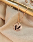 A person wearing a grey sweater and a necklace with an engraved footprint pendant on a chain.
