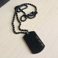 Black dog tag pendant on a chain against a beige background