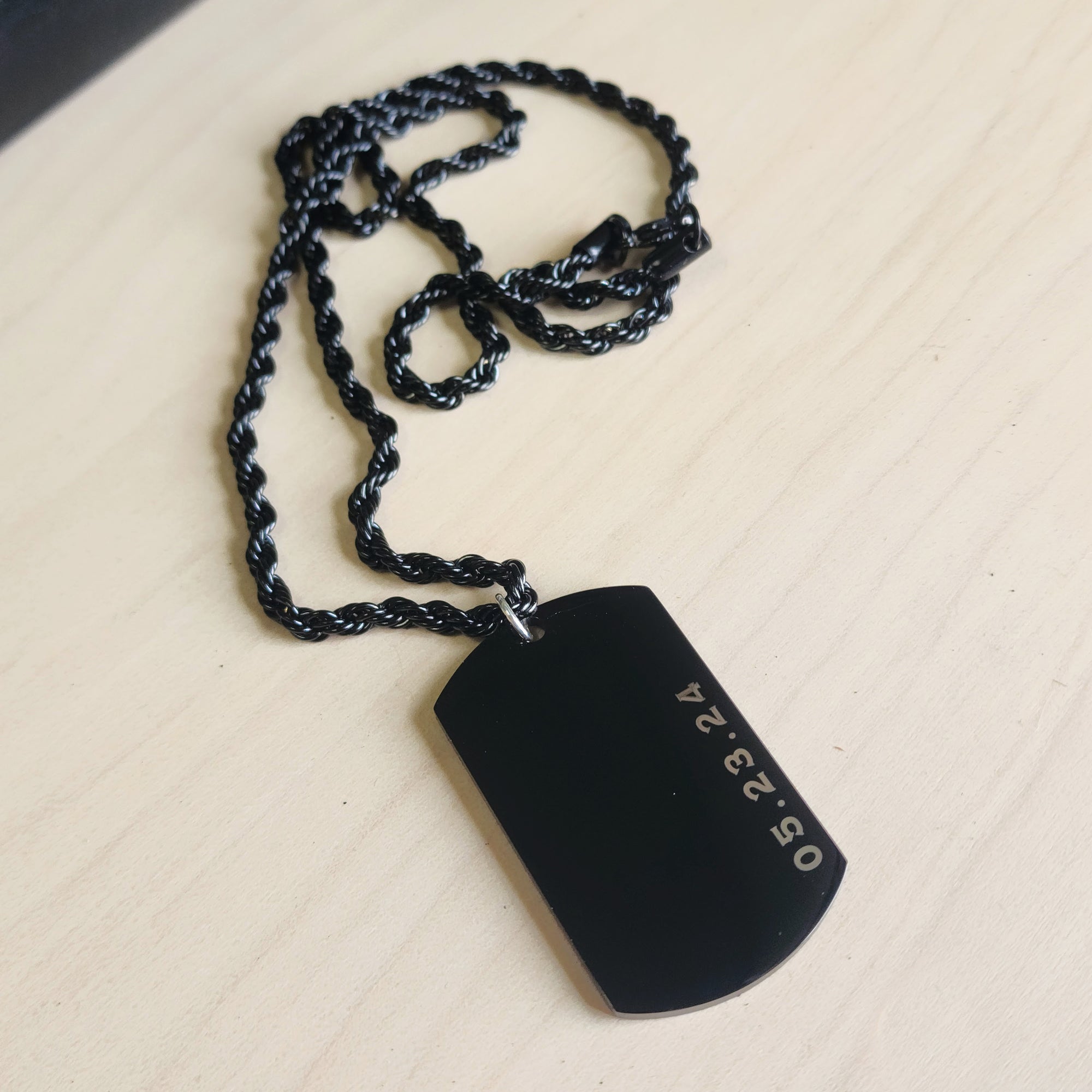 Black dog tag pendant on a chain against a beige background