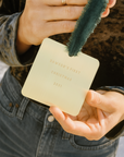 Hand holding a small square card with 'Dawson's First Christmas 2021' text, with a green felt ornament.