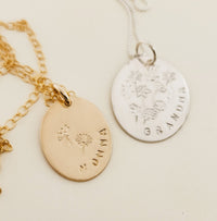 Two necklaces with gold-filled or silver round charms, one with a floral design and the other with a more detailed floral wreath design, attached to small gold or silver chains.