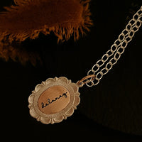 Gold necklace with a round pendant engraved with 'balance' on a dark background.