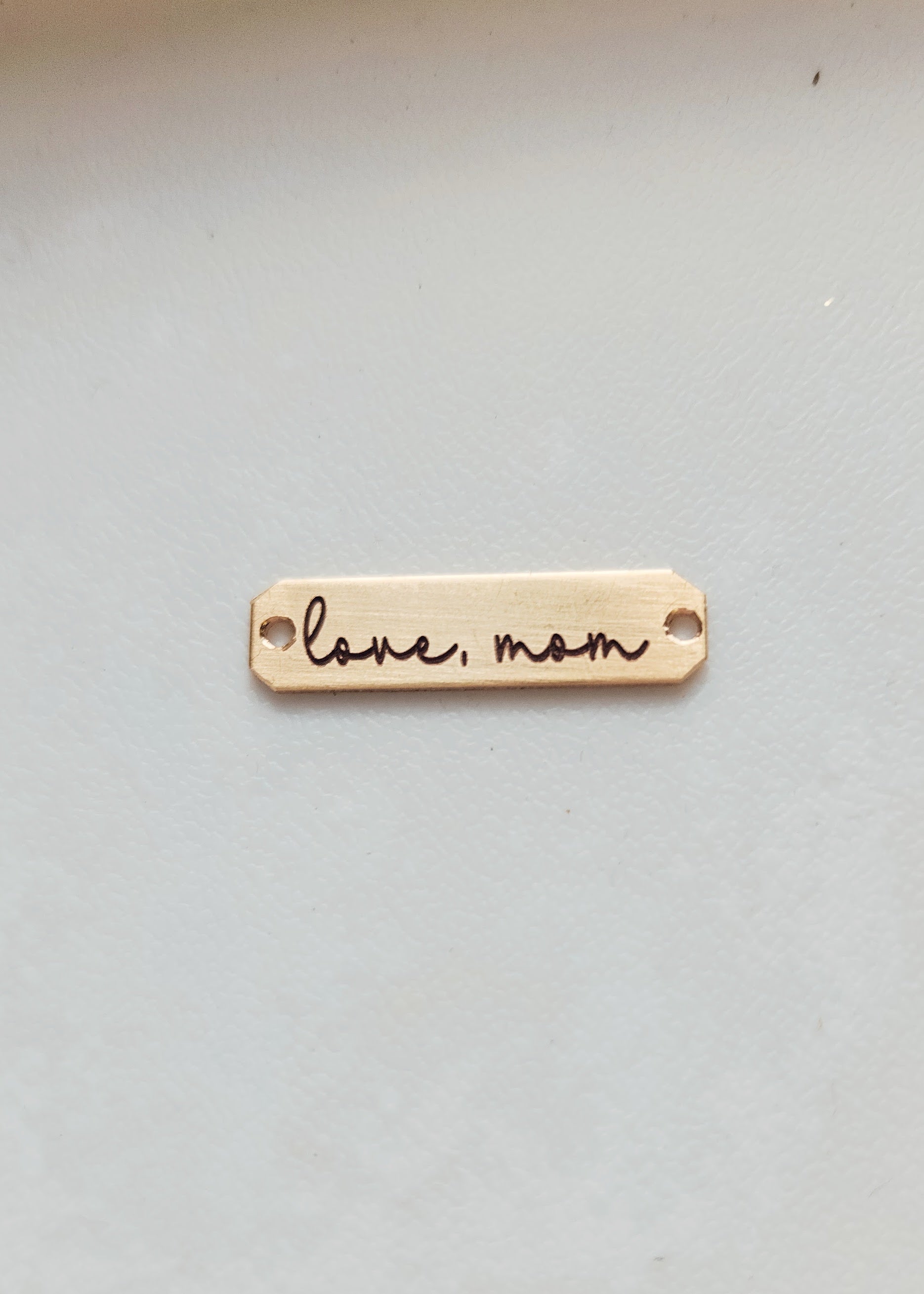 A double-sided wooden handwriting connector bar with the inscription 'Love Mom' engraved on it, placed on a white surface.