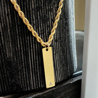 Gold necklace with a rectangular pendant on a wooden surface