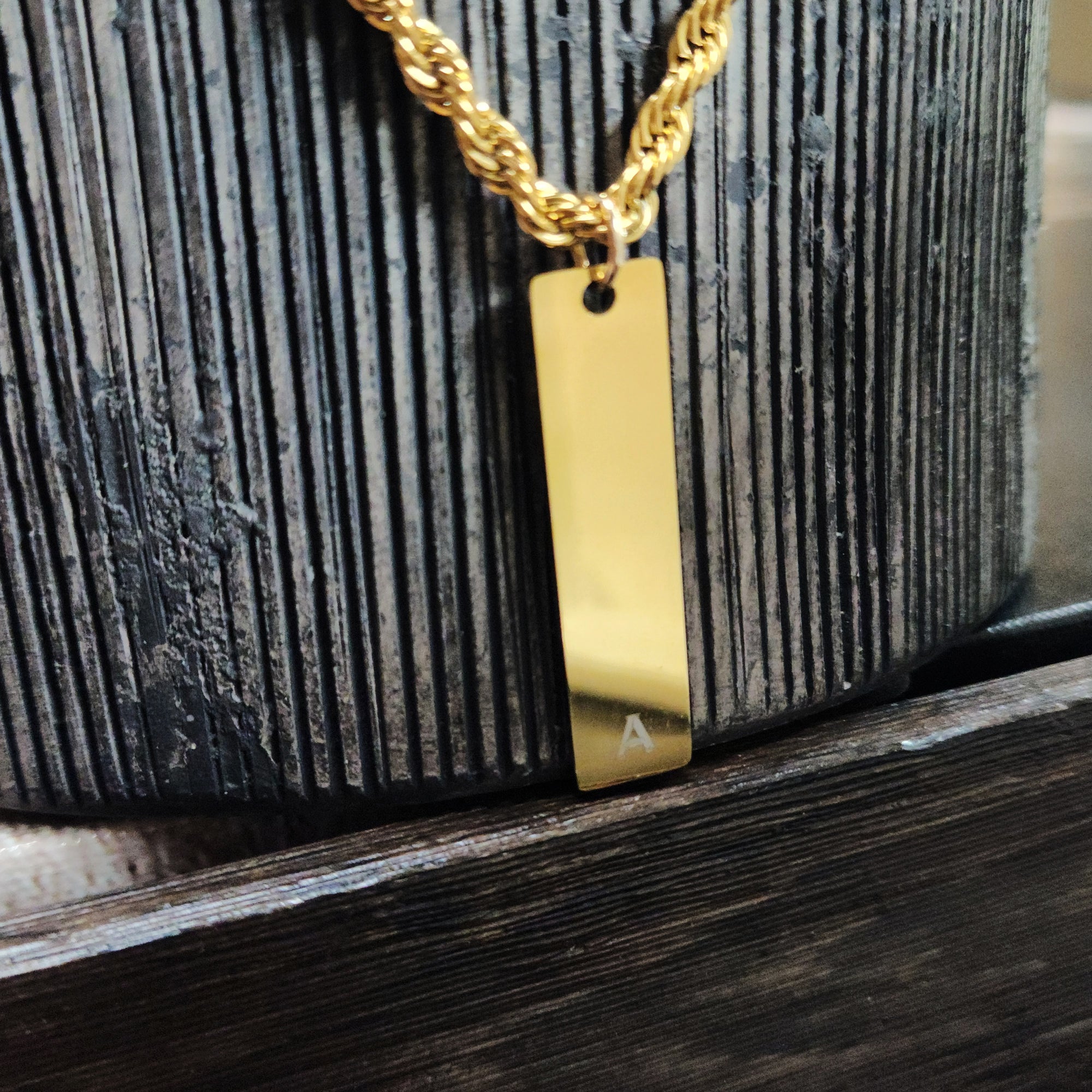Gold necklace with a rectangular pendant on a textured surface
