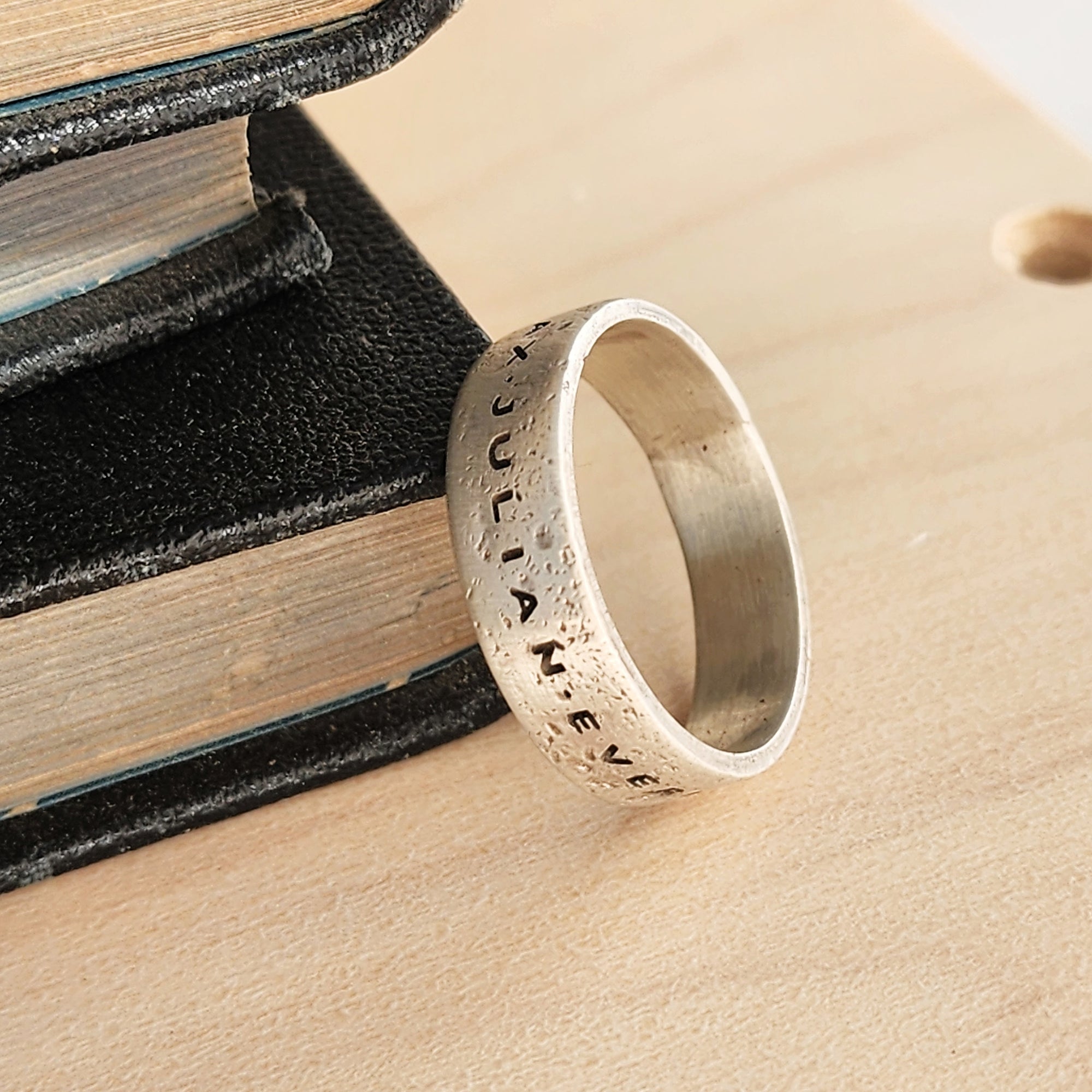 Silver ring with engraved text on a textured surface with books in the background