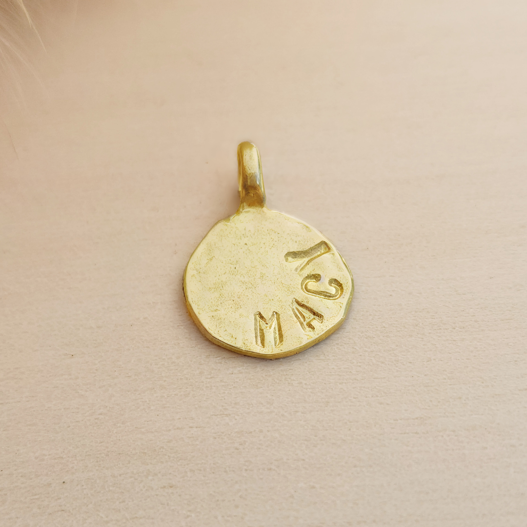 Gold pendant with engraved text on a beige background