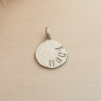 Silver pendant with 'Macy' engraved on a beige background
