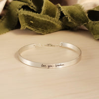 silver cuff bracelet on wood with green ribbon in background