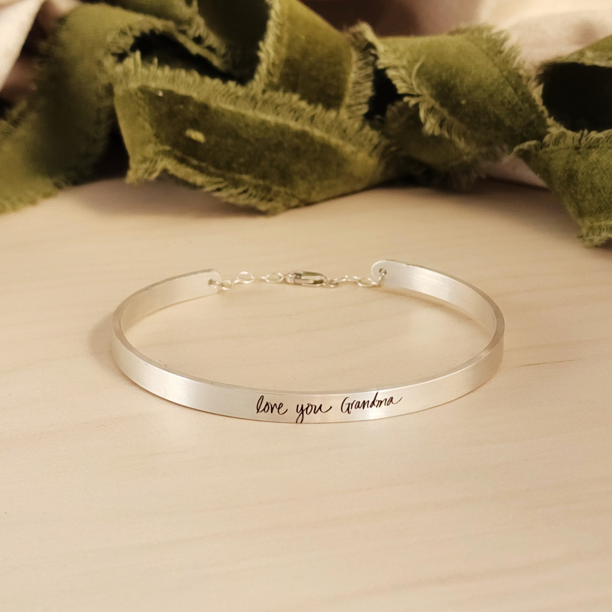 silver cuff bracelet on wood with green ribbon in background