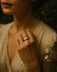 Close-up of a person wearing a gold ring with a blurred natural background